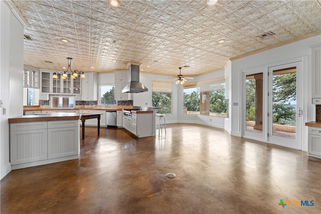 kitchen with wooden counters, pendant lighting, wall chimney exhaust hood, and stainless steel appliances