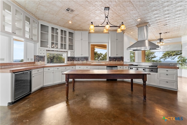 kitchen with island exhaust hood, wooden counters, decorative light fixtures, decorative backsplash, and beverage cooler