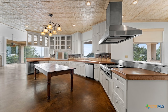 kitchen featuring white cabinetry, stainless steel appliances, decorative light fixtures, and wall chimney range hood