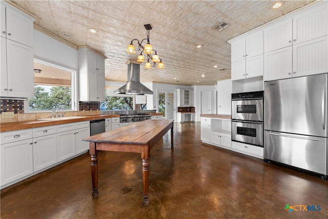 kitchen featuring stainless steel appliances, wall chimney range hood, backsplash, decorative light fixtures, and white cabinets