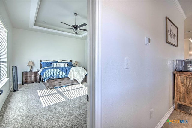 bedroom featuring a tray ceiling, ornamental molding, ceiling fan, and carpet