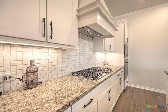 kitchen with crown molding, custom range hood, white cabinets, and appliances with stainless steel finishes