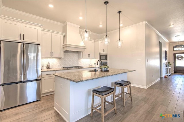 kitchen with appliances with stainless steel finishes, a center island with sink, custom range hood, white cabinets, and stone countertops