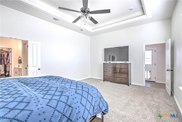 carpeted bedroom featuring a closet, a walk in closet, ceiling fan, and a tray ceiling