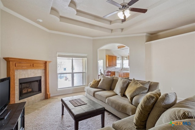 living room with a fireplace, ceiling fan, crown molding, and a tray ceiling