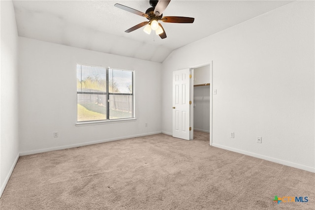 unfurnished bedroom featuring ceiling fan, light colored carpet, a spacious closet, and vaulted ceiling