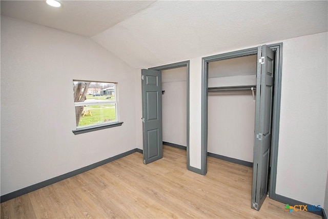 unfurnished bedroom with light wood-type flooring, lofted ceiling, a textured ceiling, and two closets