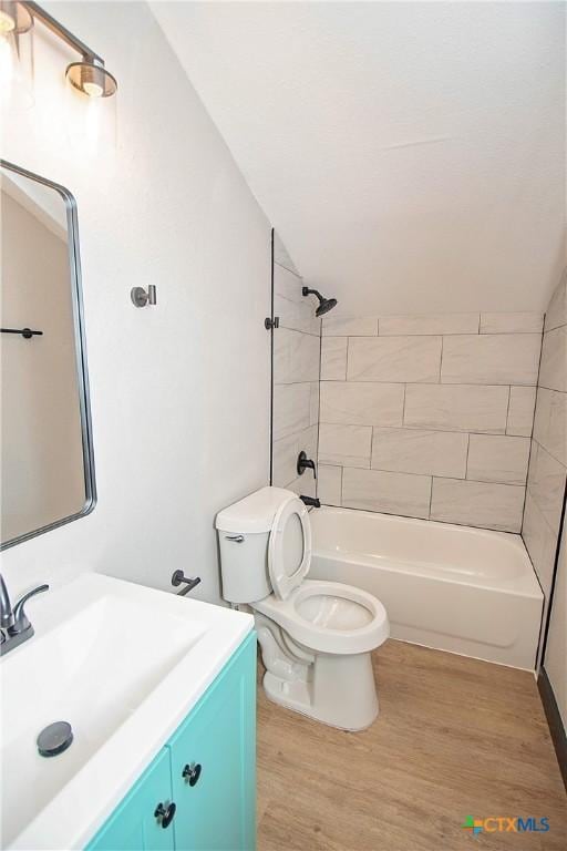 full bathroom featuring vanity, lofted ceiling, hardwood / wood-style flooring, tiled shower / bath combo, and toilet