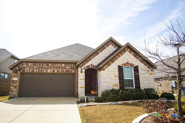 french country home with driveway, stone siding, roof with shingles, an attached garage, and brick siding