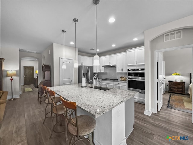 kitchen featuring arched walkways, a sink, white cabinets, appliances with stainless steel finishes, and decorative light fixtures