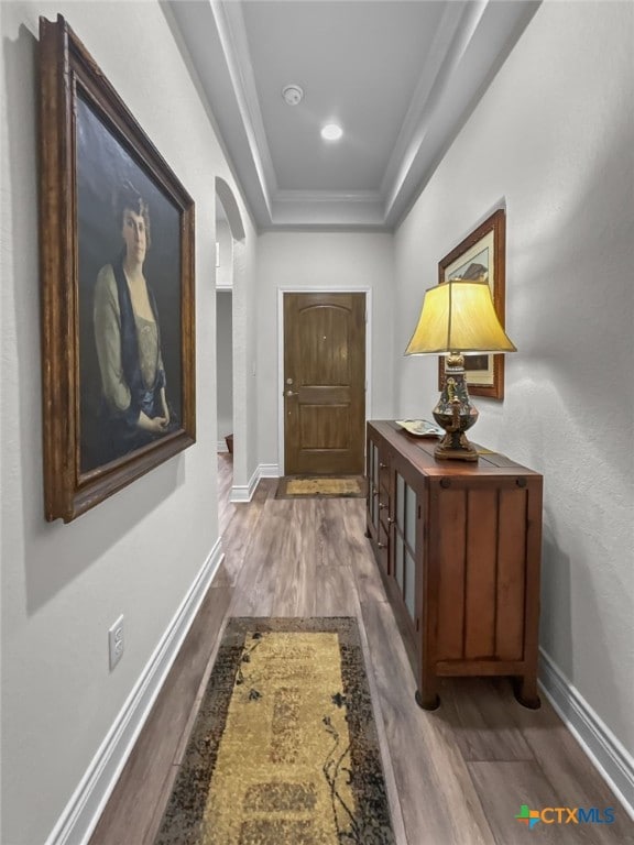 doorway to outside with arched walkways, a raised ceiling, wood finished floors, and baseboards