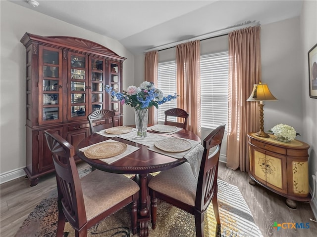 dining room featuring vaulted ceiling, wood finished floors, and baseboards