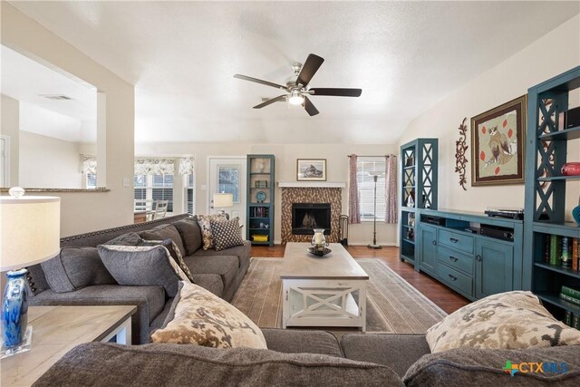 living area featuring visible vents, lofted ceiling, a fireplace, dark wood-style floors, and a ceiling fan