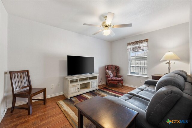 living area featuring a ceiling fan, baseboards, and wood finished floors