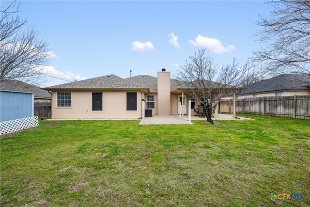 rear view of property with stucco siding, a lawn, a chimney, a fenced backyard, and a patio