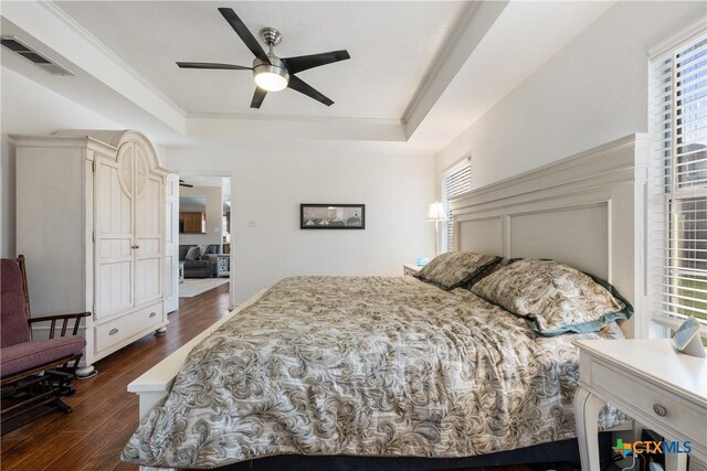 bedroom with a tray ceiling, multiple windows, dark wood-type flooring, and visible vents