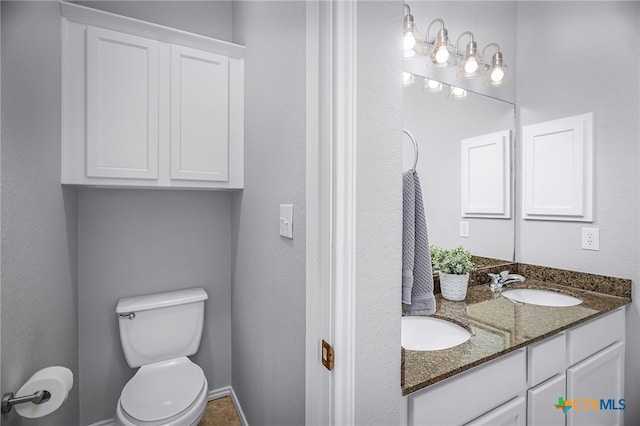 bathroom with toilet, baseboards, double vanity, and a sink