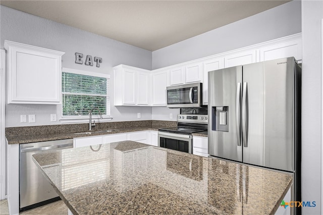 kitchen featuring white cabinetry, stainless steel appliances, dark stone countertops, and a sink