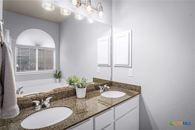 full bath with double vanity, a textured wall, a garden tub, and a sink