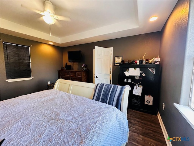 bedroom with ceiling fan, dark hardwood / wood-style flooring, and a raised ceiling