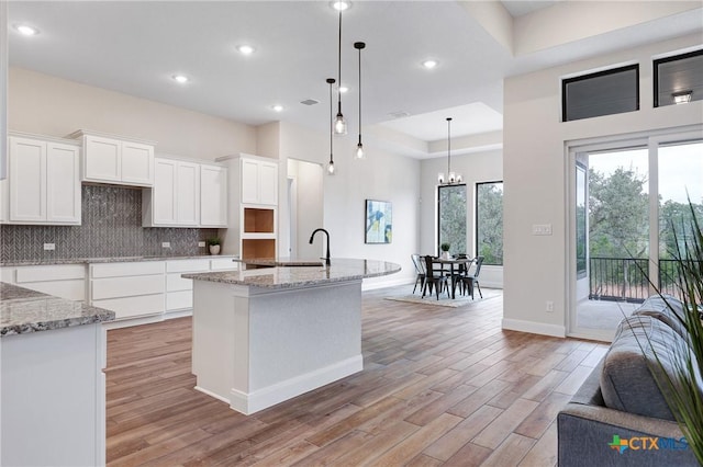 kitchen featuring tasteful backsplash, hanging light fixtures, a kitchen island with sink, light hardwood / wood-style floors, and white cabinets