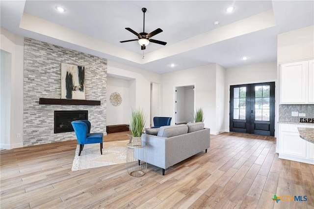 living room with french doors, a large fireplace, a raised ceiling, and light hardwood / wood-style floors