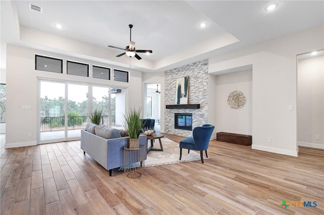 living room featuring ceiling fan, a stone fireplace, and a raised ceiling