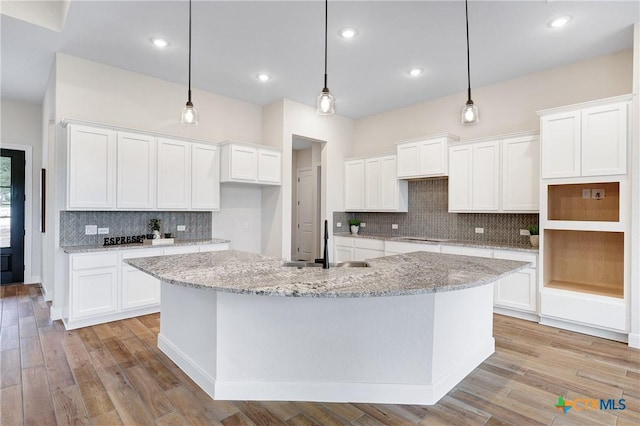 kitchen featuring hanging light fixtures, light stone countertops, white cabinets, and a center island with sink