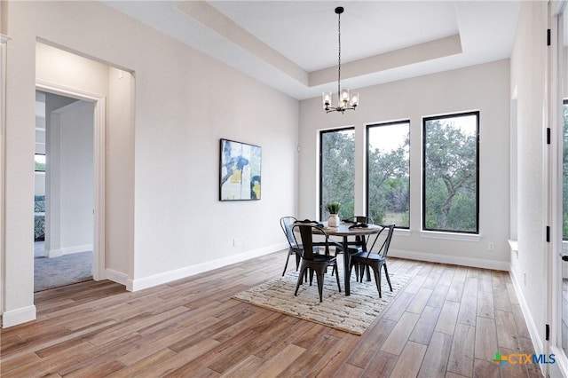 dining area with a notable chandelier, a tray ceiling, and light hardwood / wood-style floors