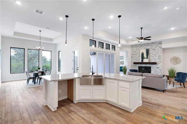 kitchen with an island with sink, a raised ceiling, sink, and white cabinets