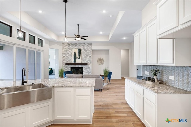 kitchen with hanging light fixtures, a stone fireplace, sink, and white cabinets