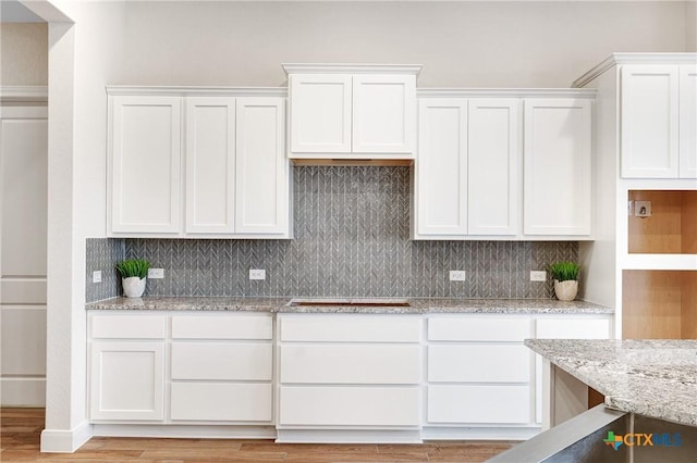 kitchen with cooktop, white cabinetry, light stone countertops, and light hardwood / wood-style floors