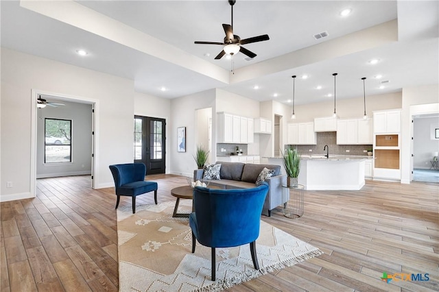 living room featuring sink, light hardwood / wood-style floors, french doors, and ceiling fan