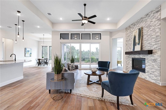 living room with a stone fireplace, a raised ceiling, and light hardwood / wood-style flooring