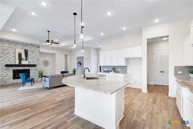 kitchen featuring a fireplace, sink, white cabinets, light stone counters, and a center island with sink