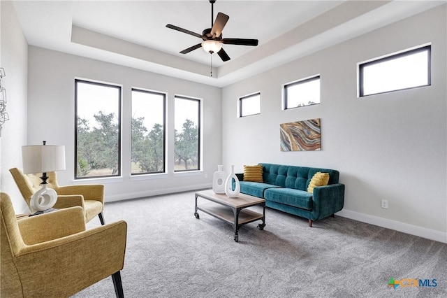 living room featuring a raised ceiling, light carpet, and ceiling fan