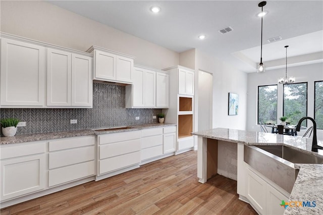 kitchen with light stone counters, sink, pendant lighting, and white cabinets