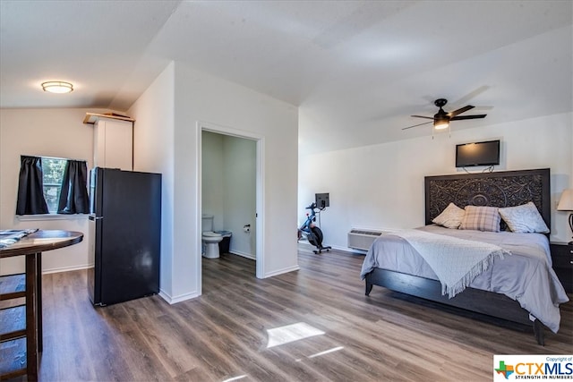 bedroom featuring ceiling fan, a wall mounted air conditioner, ensuite bathroom, wood-type flooring, and black refrigerator