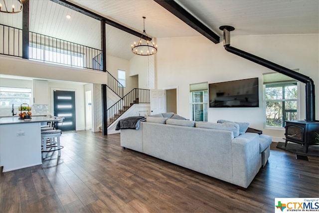 living room with beamed ceiling, dark wood-type flooring, a wood stove, and a notable chandelier