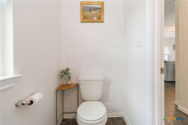 bathroom with wood-type flooring, brick wall, and toilet