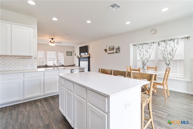 kitchen with dark hardwood / wood-style flooring, dishwasher, sink, a kitchen island, and white cabinetry