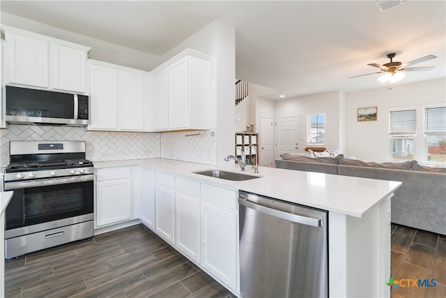 kitchen featuring stainless steel appliances, sink, kitchen peninsula, white cabinets, and dark wood-type flooring