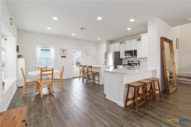 kitchen featuring stainless steel appliances, white cabinetry, a breakfast bar, dark hardwood / wood-style flooring, and decorative backsplash