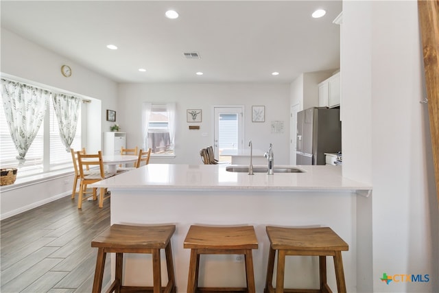 kitchen with dark hardwood / wood-style flooring, kitchen peninsula, sink, a kitchen breakfast bar, and stainless steel refrigerator