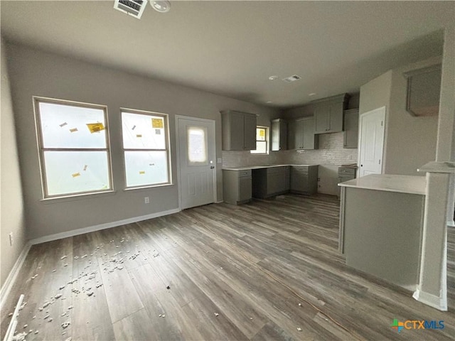 kitchen with baseboards, gray cabinetry, visible vents, decorative backsplash, and wood finished floors
