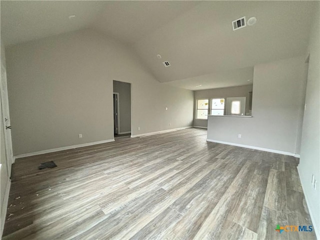 unfurnished living room featuring wood finished floors, baseboards, lofted ceiling, and visible vents
