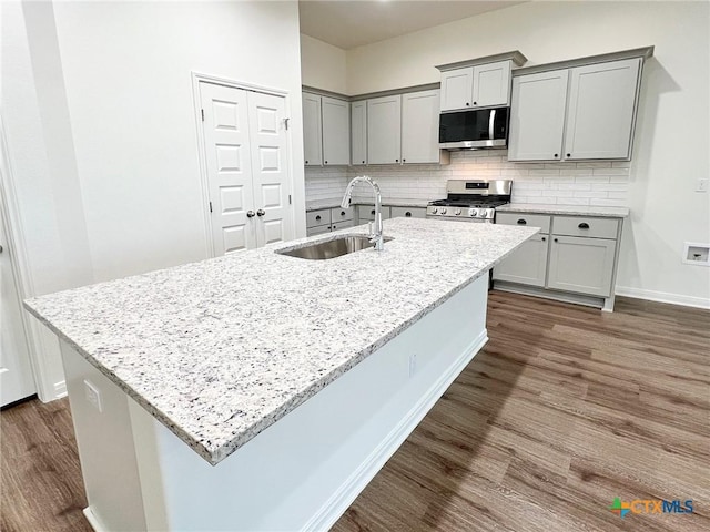 kitchen featuring sink, light stone countertops, an island with sink, and appliances with stainless steel finishes