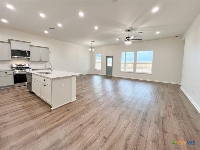 kitchen featuring sink, appliances with stainless steel finishes, backsplash, light stone counters, and a center island with sink