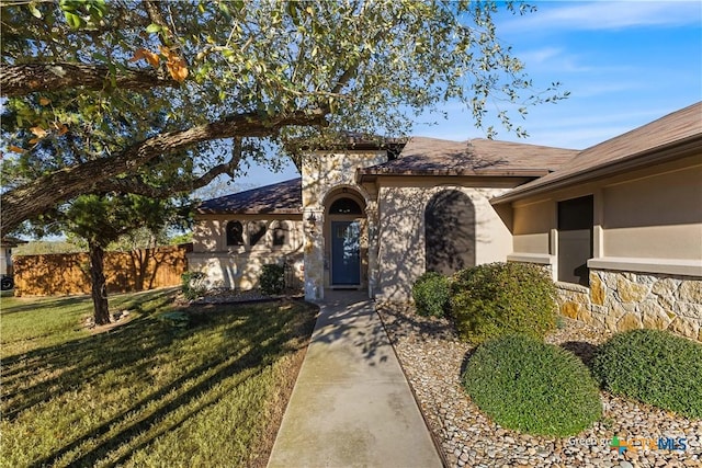 view of front of home with stucco siding, stone siding, a front yard, and fence