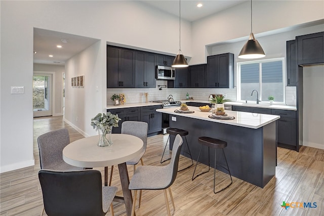 kitchen with stainless steel appliances, backsplash, hanging light fixtures, light hardwood / wood-style floors, and a center island